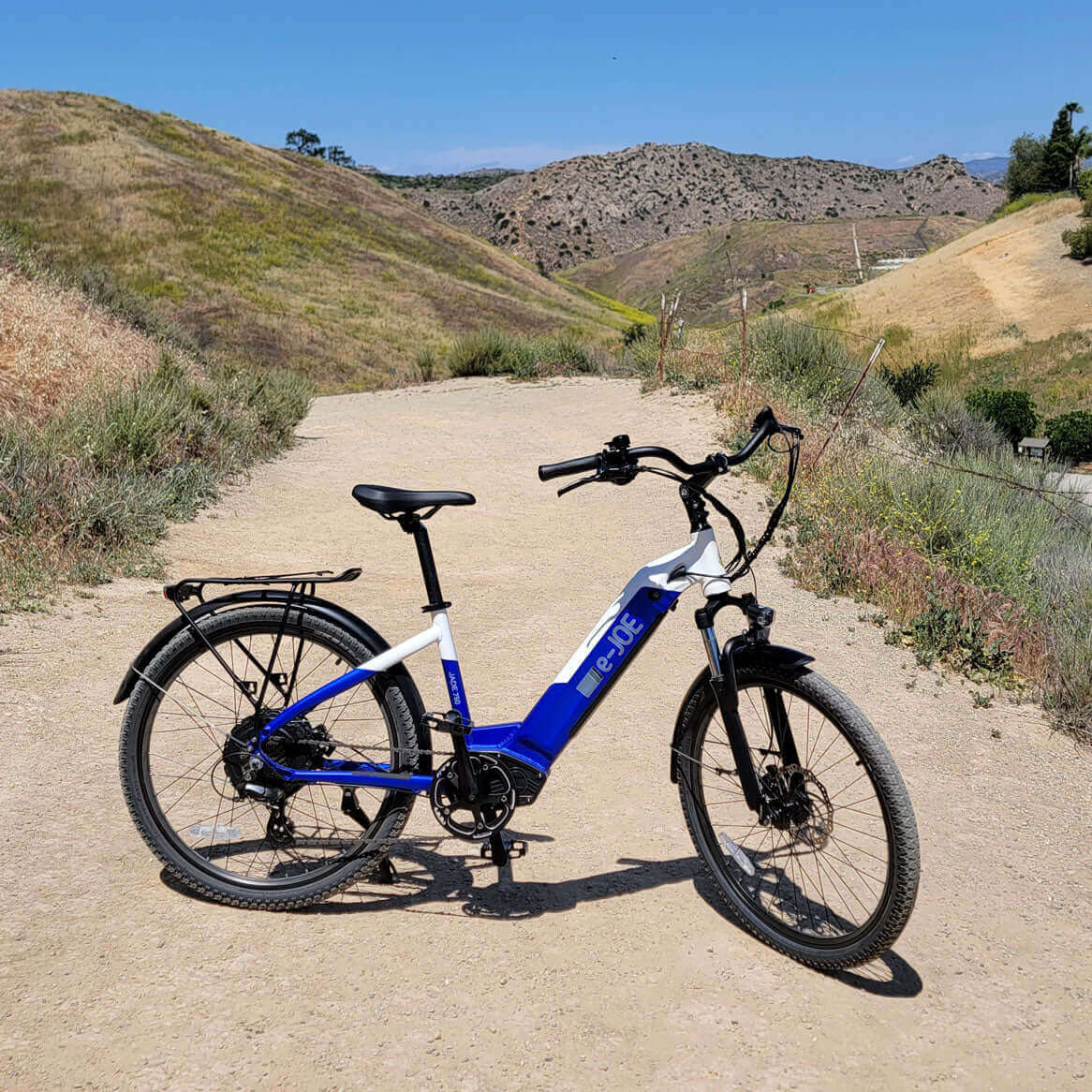 E-Joe Jade Beach Cruiser electric bike parked on a dirt path surrounded by hills.