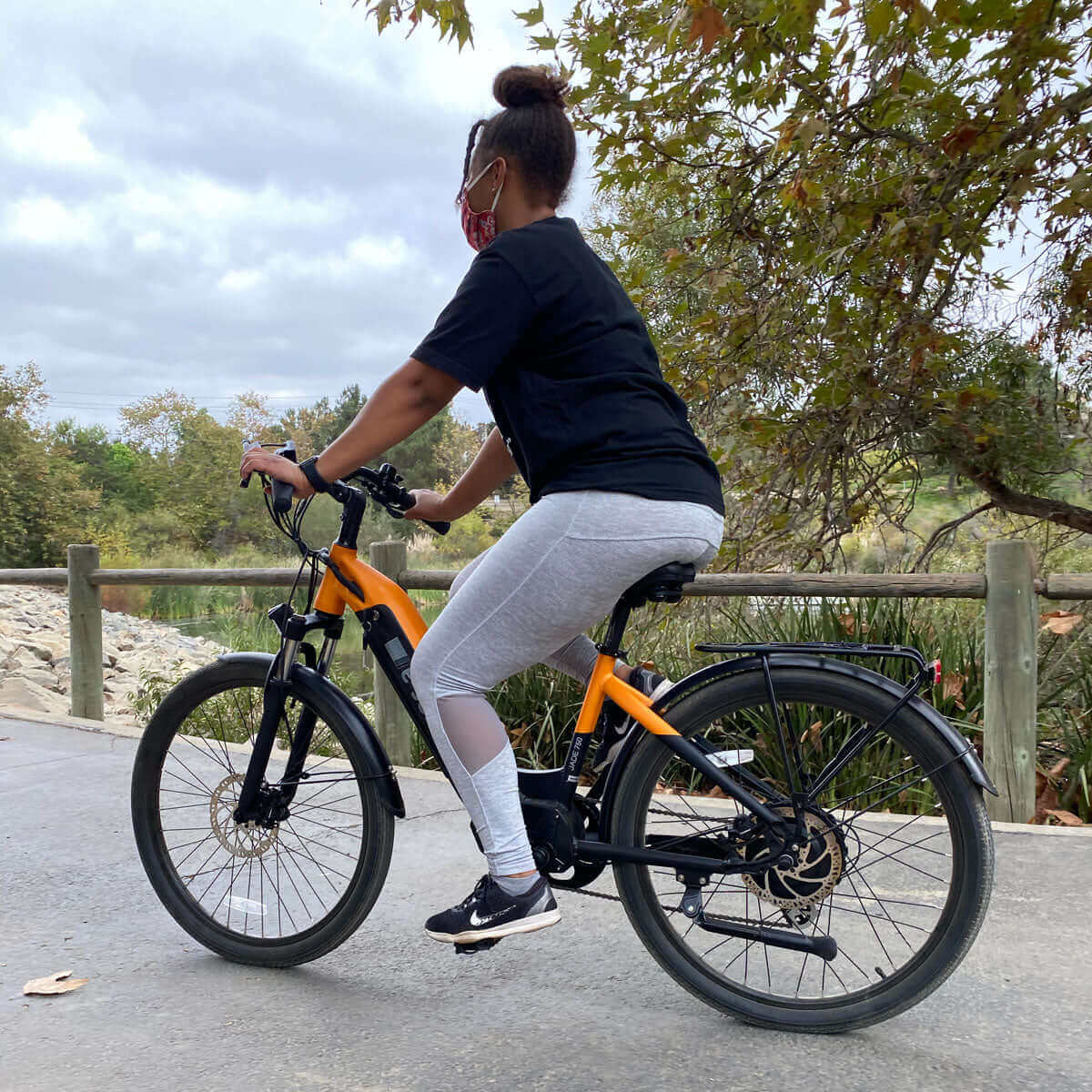 Person riding an electric bike on a scenic pathway wearing a mask and comfortable athletic wear.