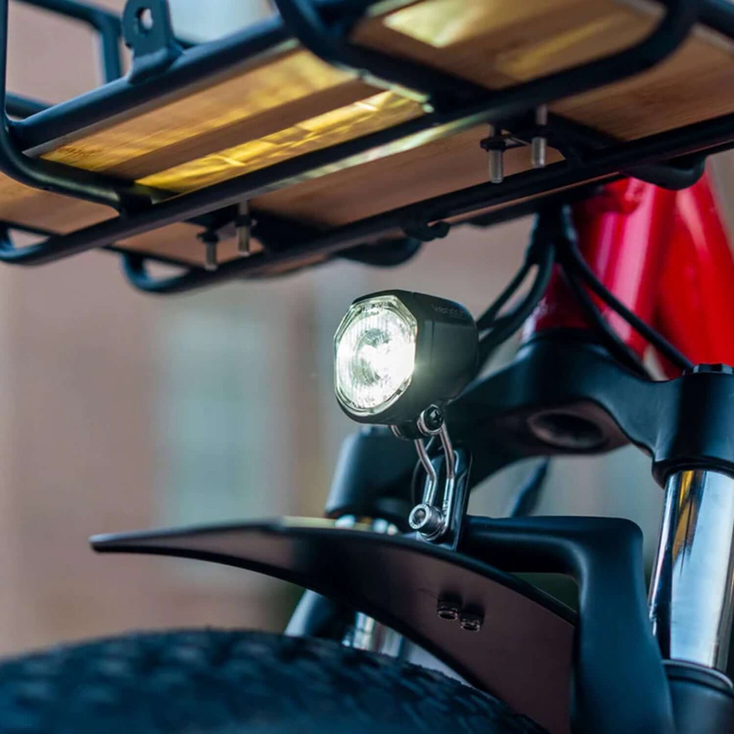 Close-up of a bike light mounted on a red electric trike, illuminating the front wheel and fender.