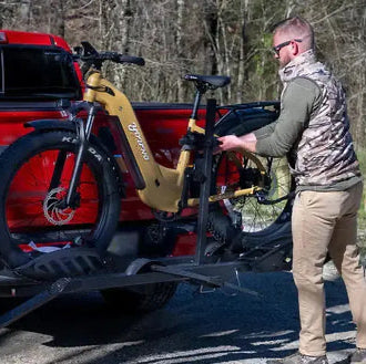 Person loading a bicycle onto a red pickup truck with a bike rack.