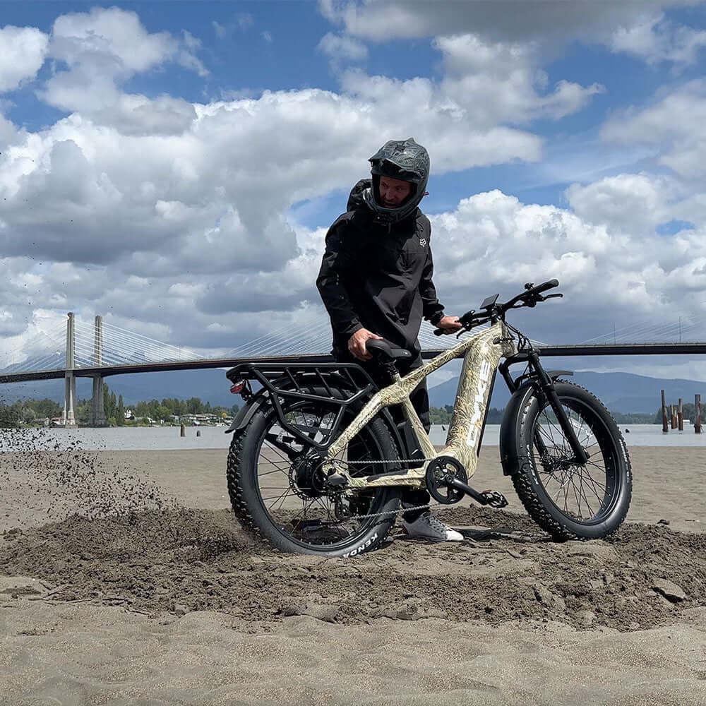 Person on an electric bike on a sandy beach with a bridge and mountains in the background