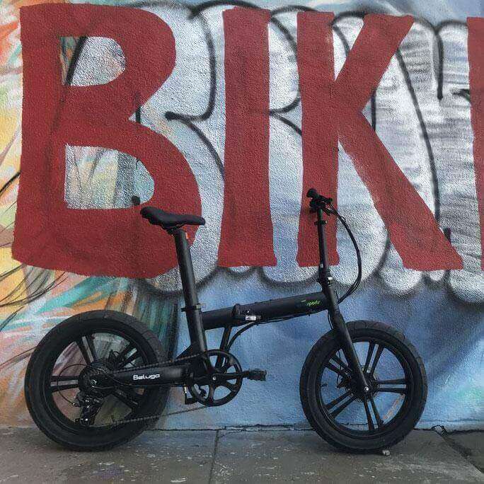 Qualisports Beluga STD/PLUS fat tire folding electric bike in front of a colorful 'BIKE' graffiti wall.