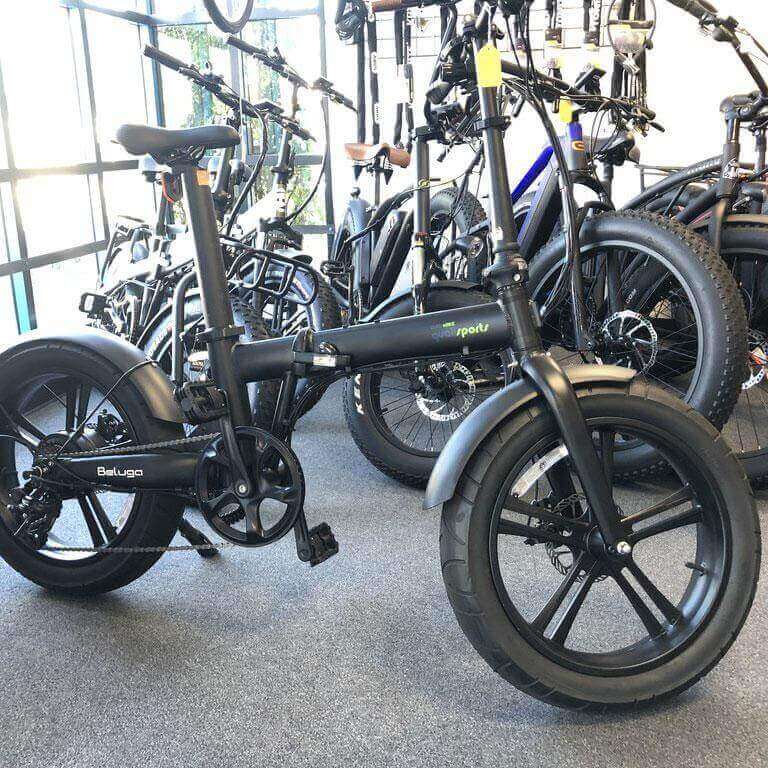 Qualisports Beluga STD/PLUS fat tire folding electric bike displayed in a shop, showcasing sleek design and robust tires.