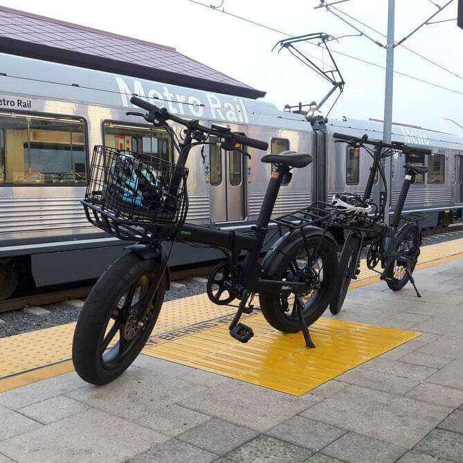 Qualisports Beluga fat tire folding electric bike parked on a train station platform next to a Metro Rail train.
