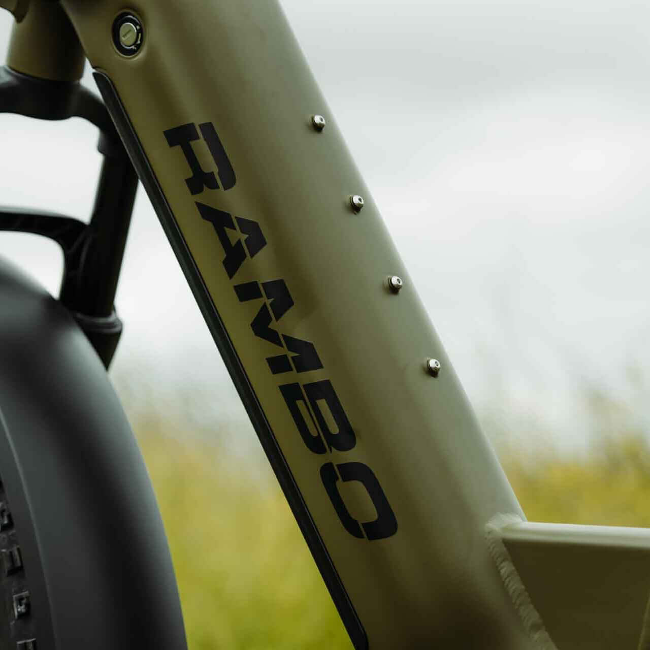 Close-up of a bicycle frame with 'RAMBO' branding against a blurred natural background