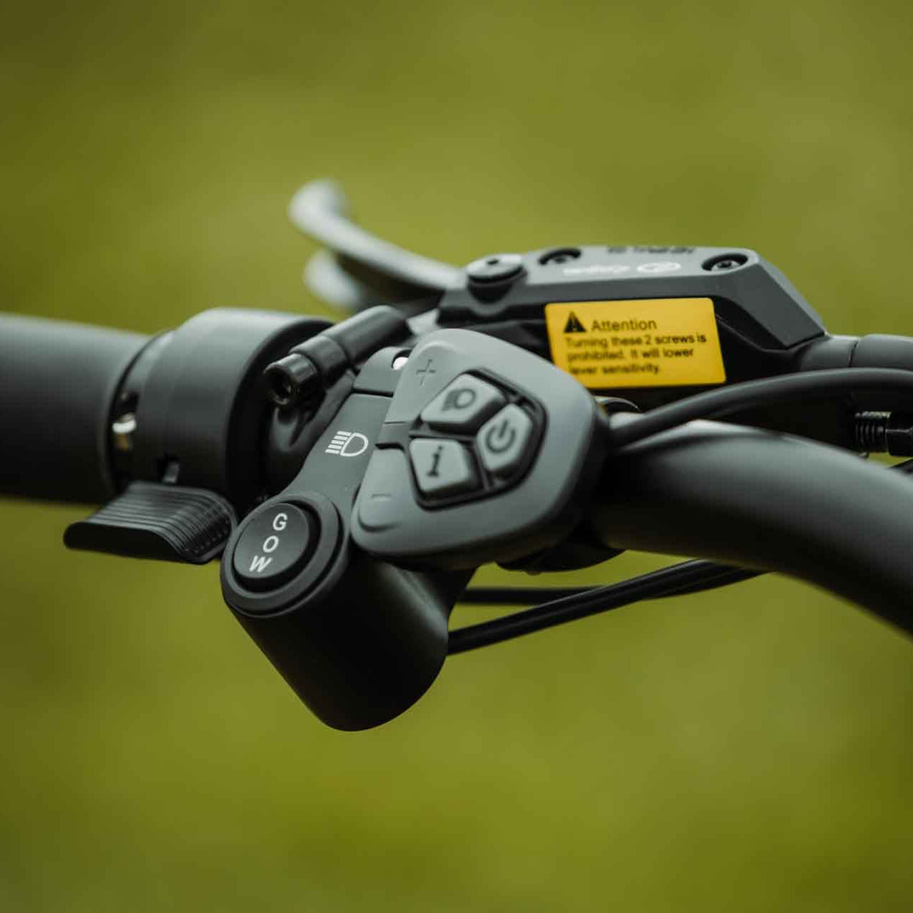 Close-up of a motorcycle handlebar control panel with buttons and a warning label on a blurred background.