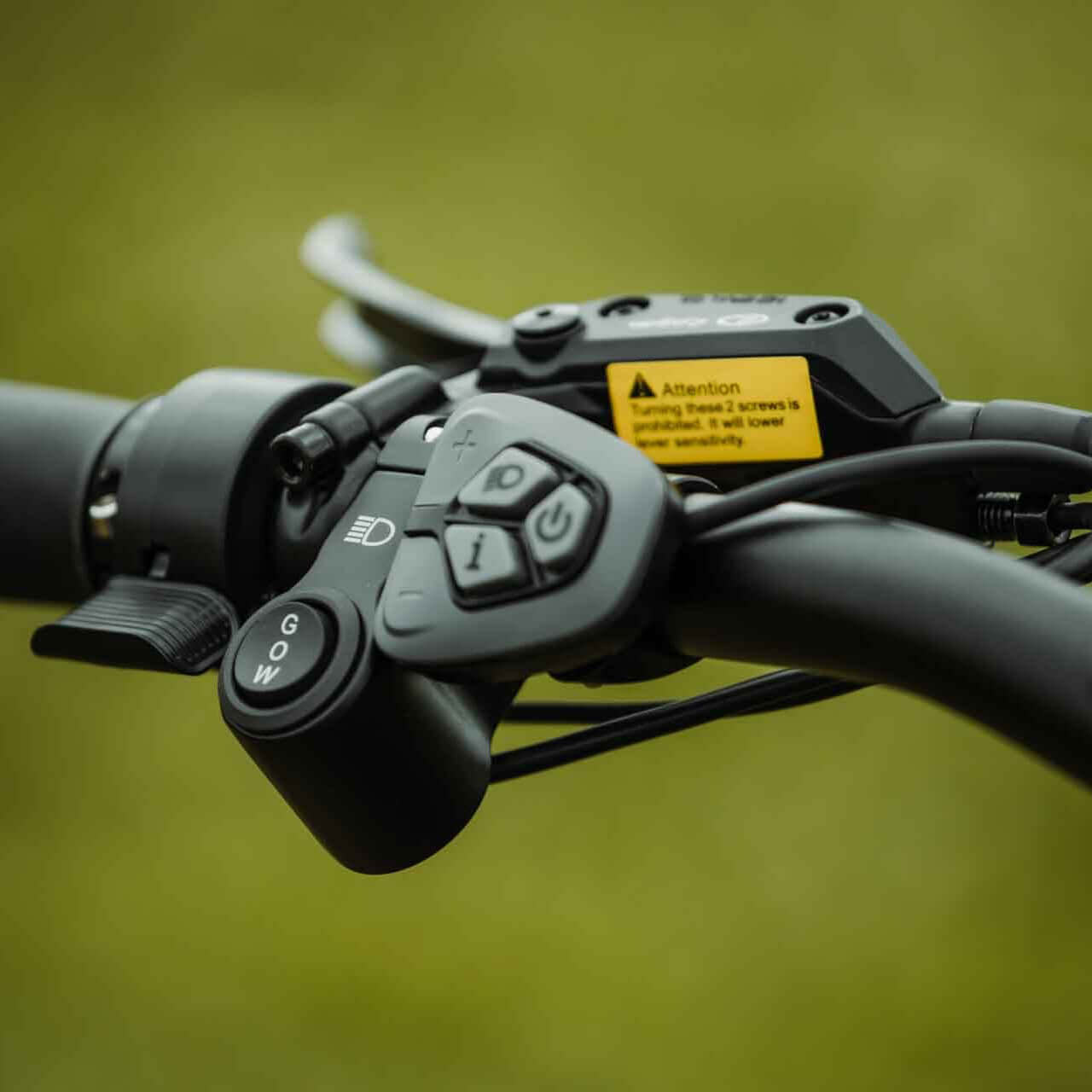 Close-up of a motorcycle handlebar control panel with buttons and a warning label on a blurred background.