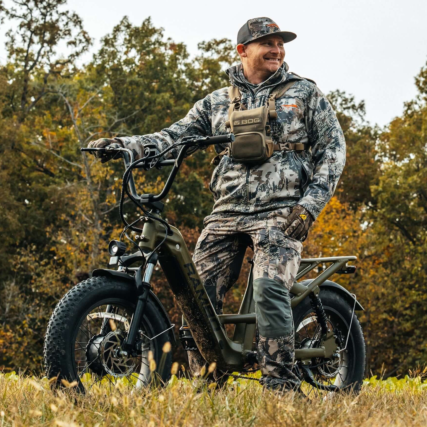 Man in camouflage gear standing next to an electric bike in a forest setting