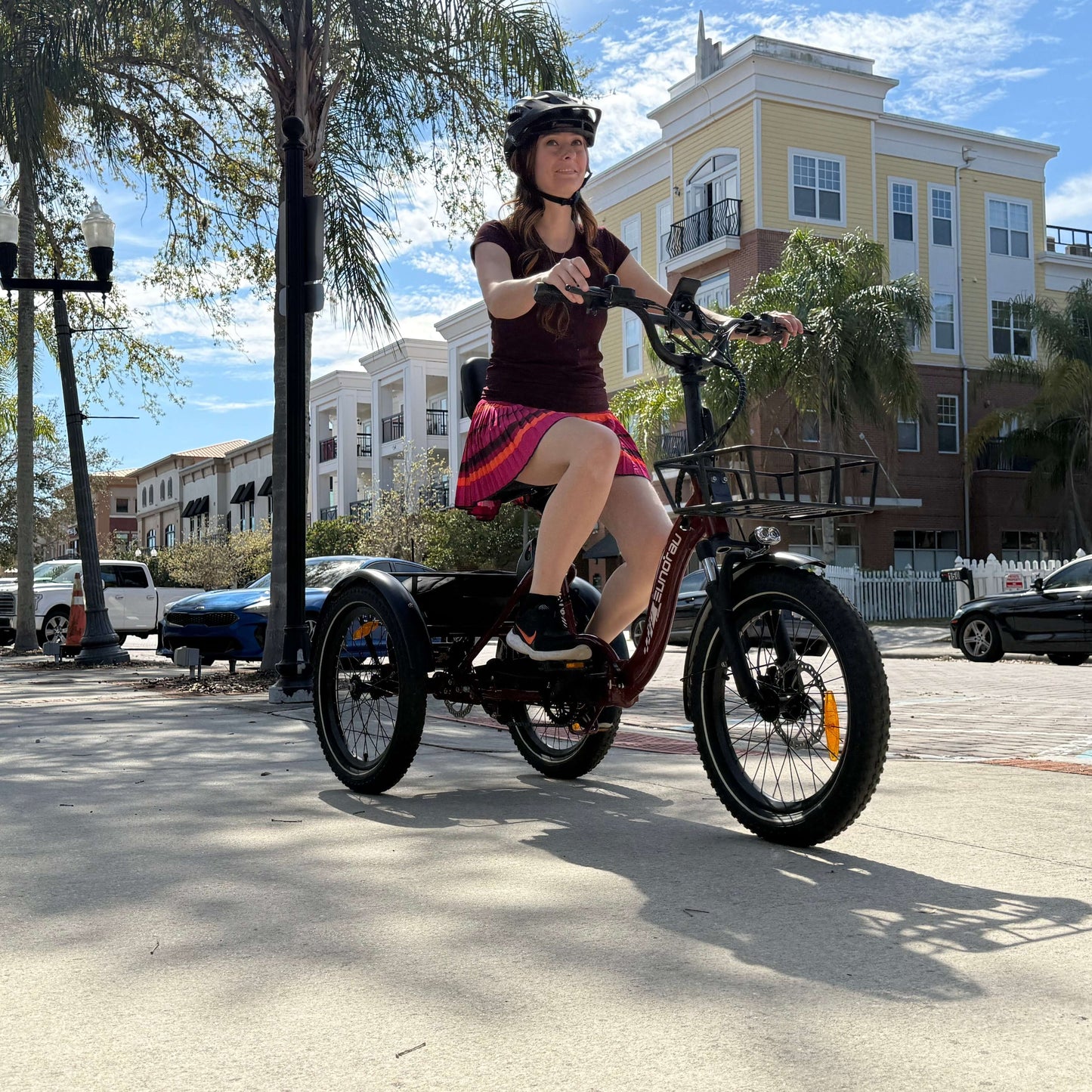 Person riding a tricycle on a street with palm trees and buildings in the background