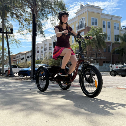 Person riding a tricycle on a street with palm trees and buildings in the background