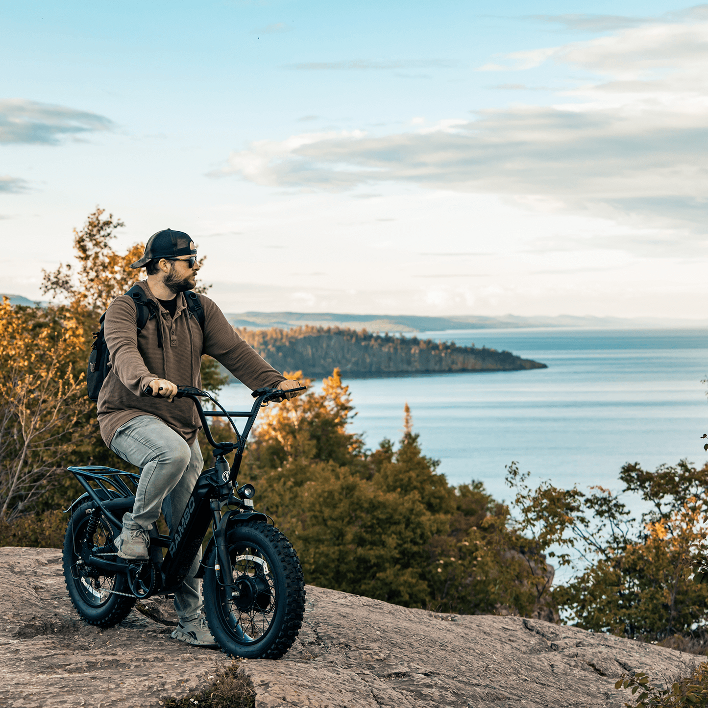 Person riding a bike on a rocky outcrop with a scenic view of water and trees in the background