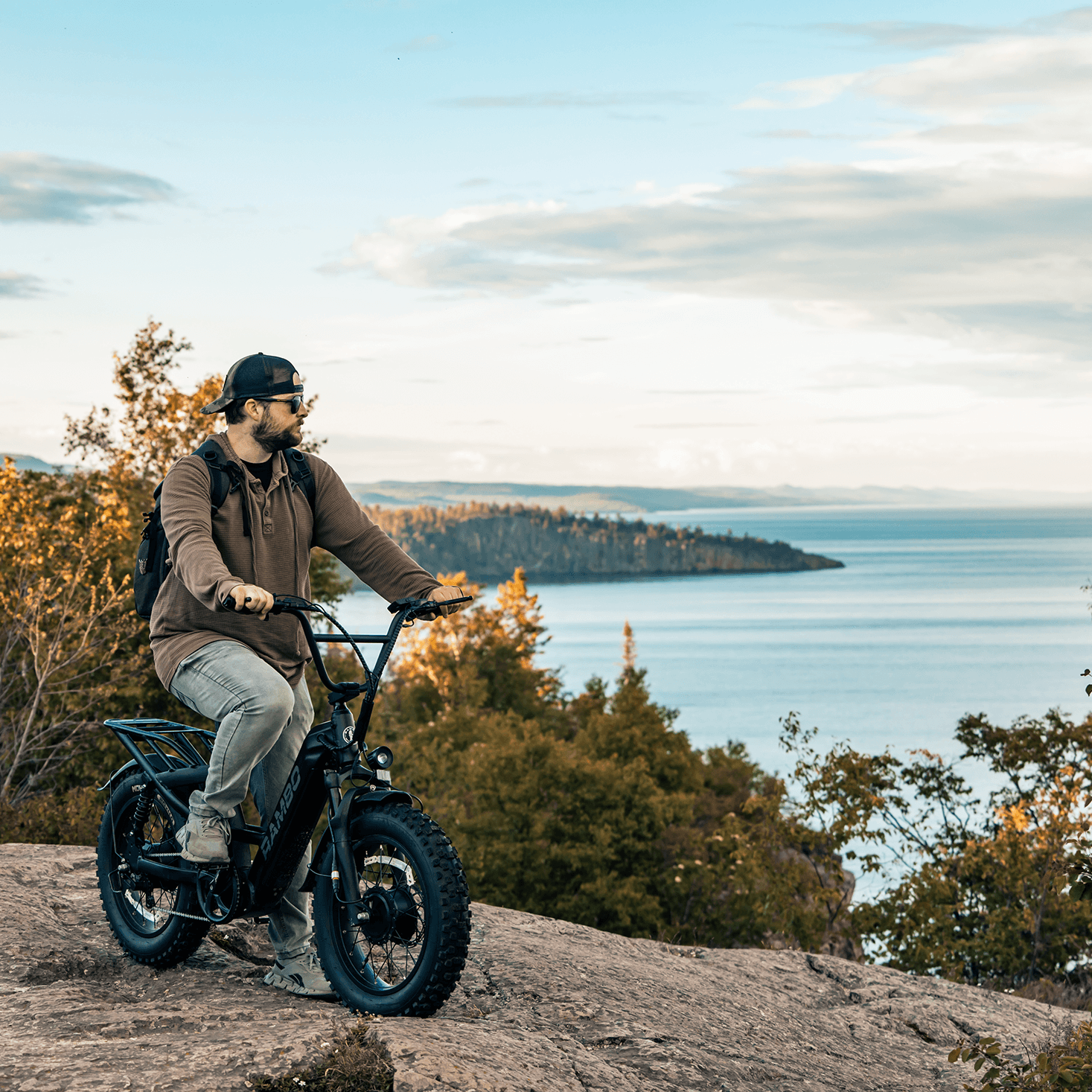 Person riding a bike on a rocky outcrop with a scenic view of water and trees in the background