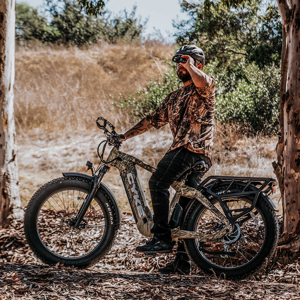 Man sitting on a motorcycle in a natural setting with trees and dry grass.